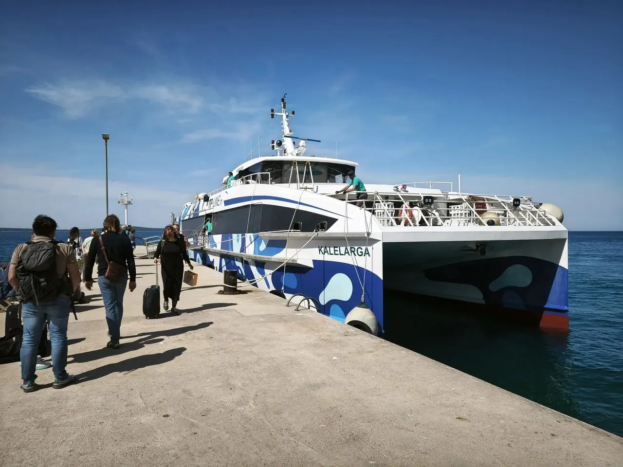 The TP Line catamaran moored at the pier on Olib, passengers walking ashore with their luggage
